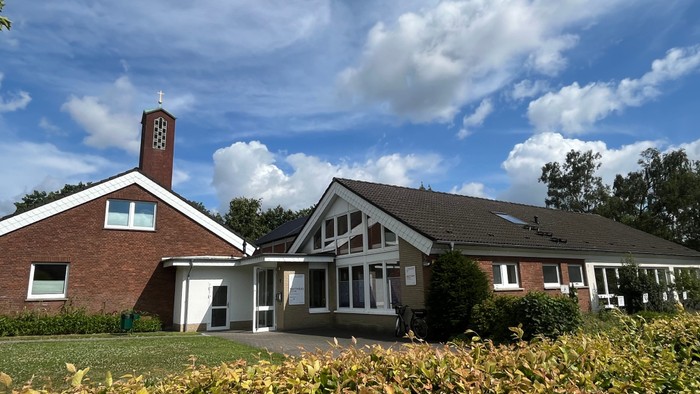 Man sieht links das rot geklinkerte Pfarrhaus, rechts schließt das Gemeindehaus mit vielen weißen Fenstern an. Im Hintergrund sieht man noch den Turm der Matthäuskirche.