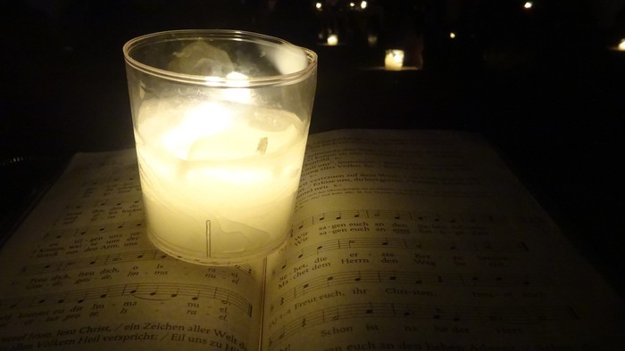 Eine Kerze in einem Glas steht auf einem aufgeschlagenen Buch bei Nacht