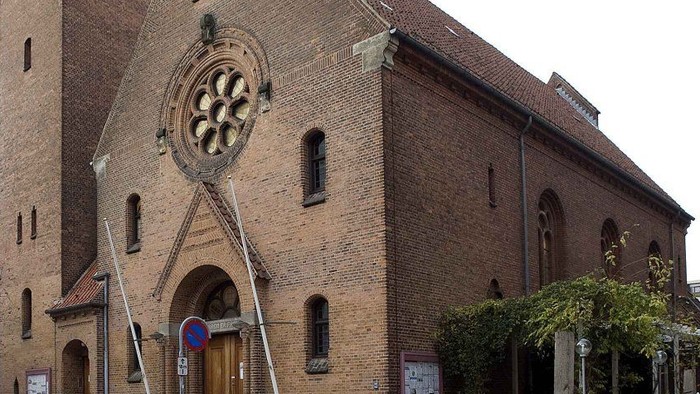 Gamle mursteinskirke med rosensvindueskår og trædør.