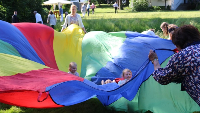 Kinder spielen in einem großen, bunten aufblasbaren Tunnel, während ein Erwachsener in der Nähe in einem Park assistiert.