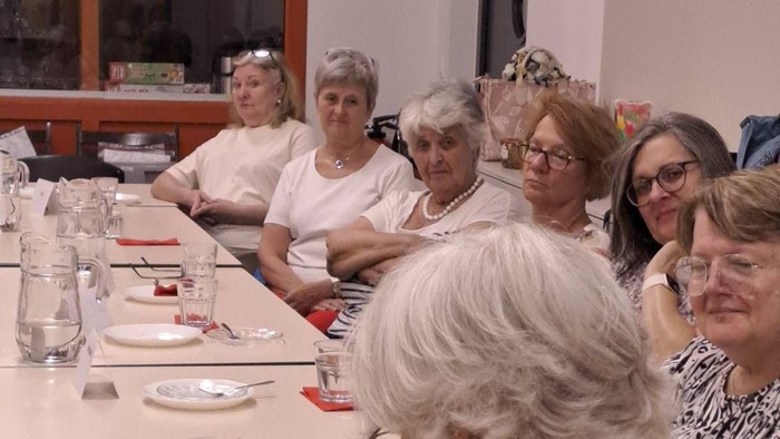 Gruppe von Frauen, die sich während eines Meetings oder einer gesellschaftlichen Veranstaltung um einen Tisch versammelt haben, wobei eine Notizen schreibt.