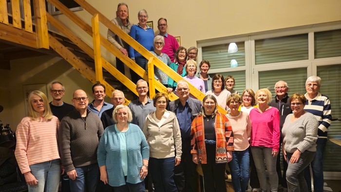 Gruppe von Menschen, die drinnen in der Nähe einer Treppe posieren und fröhlich und freundlich wirken.