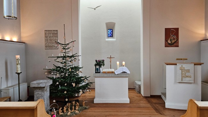 In der Kirche steht ein geschmückter Weihnachtsbaum neben einem Altar mit Kerzen.