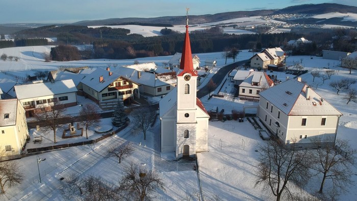 Weißer Kirchturm in verschneitem Dorf, umgeben von Bergen