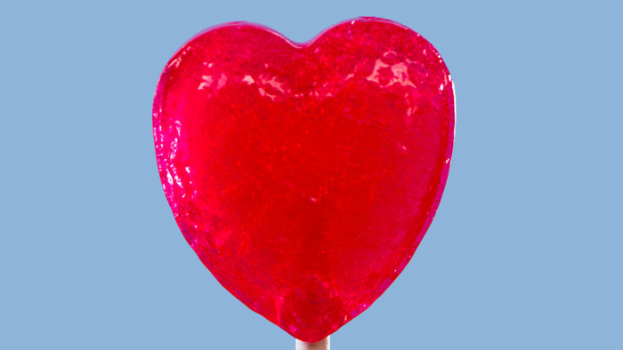 Ein glänzender, rot herzförmiger Luftballon vor blauem Hintergrund.