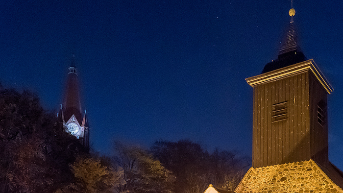Zwei Türme, einer rot und einer braun, stehen vor einem dunkelblauen Nachthimmel.