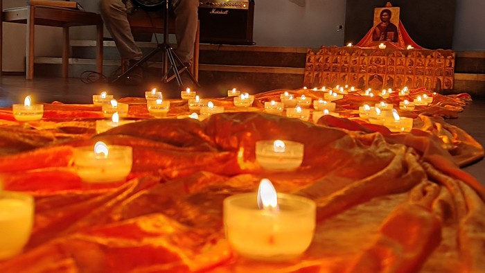 Ein Mann spielt Akkordeon während einer Gedenkfeier bei Kerzenschein, bei der zahlreiche brennende Kerzen auf einem bedeckten Tisch stehen.