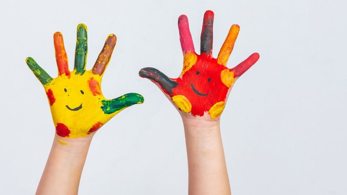 Kinderhände, bemalt mit bunten Gesichtern, vor weißem Hintergrund erhoben.