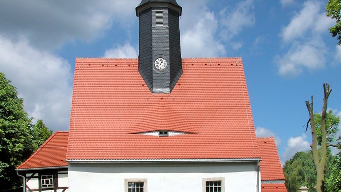 Kleine weiße Kirche mit rotem Dach und schwarzem Turm.