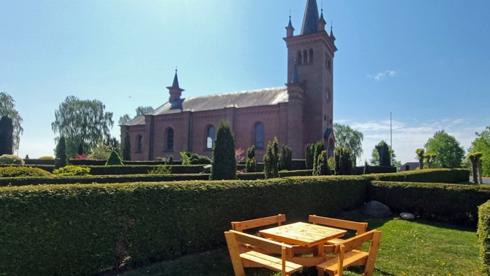 En træbord og ben ved kirkegården med en rød kirke i baggrunden