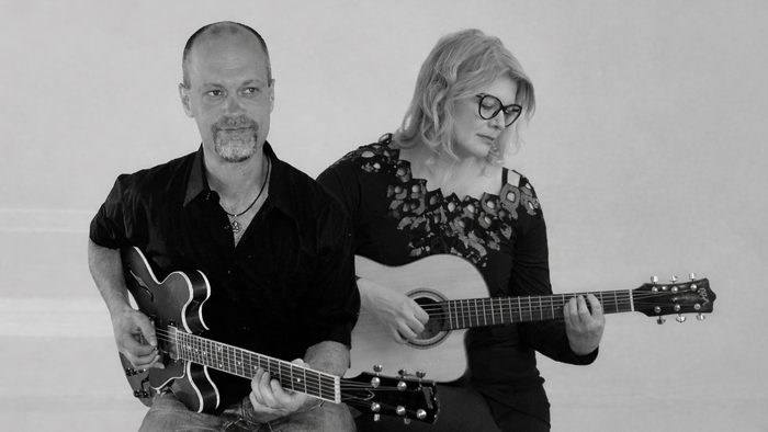 To musikere, der spiller akustiske guitarer på et sort-hvidt portræt.