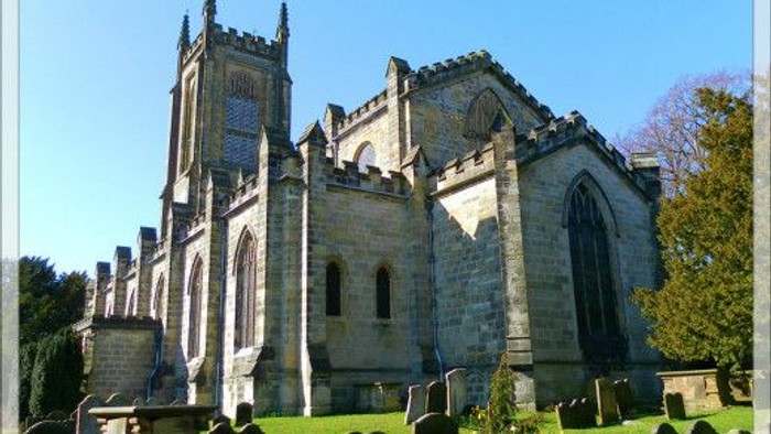 Large stone church with tall spires and arched windows, surrounded by gravestones in a cemetery.