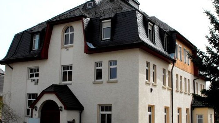 Das Bild zeigt ein zweistöckiges Gebäude mit einem Kreuz auf dem Dach.