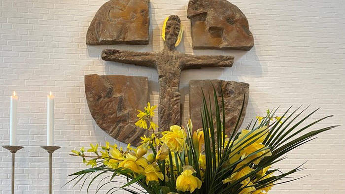 En stor blomsterarrangement med gule blomster og palmeblade foran en mur med et tårnformet reliefoverstøi.