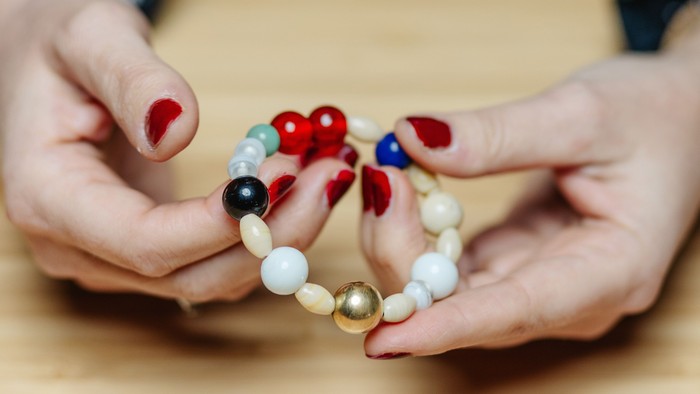 Hænder, der holder et farverigt perlearmbånd med røde, blå, sorte, hvide og gyldne perler.