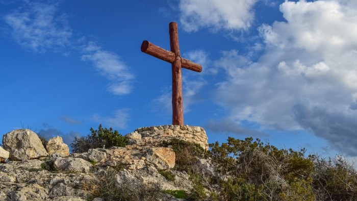 En stor trækors på en klippe med blå himmel og skyer i baggrunden