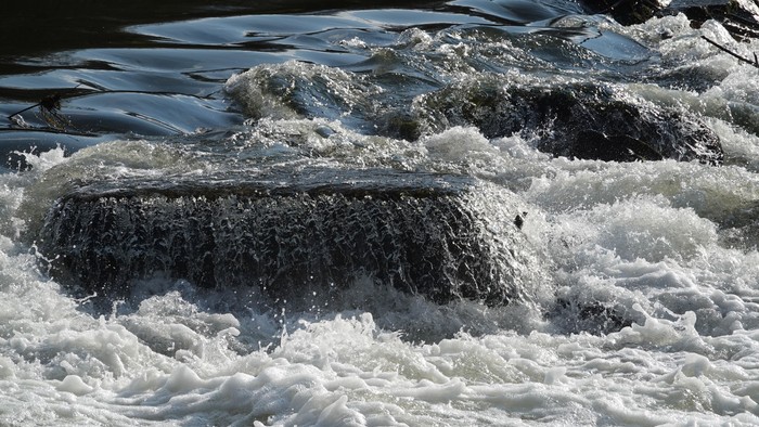 Schaumiges Wasser, das über eine felsige Oberfläche in einem natürlichen Wasserfall oder Flussstromschnellen herabstürzt.