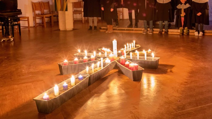 Mehrere Kerzen in Metallbehältern auf Holzboden, Menschen im Hintergrund
