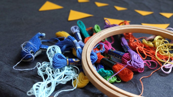 En samling bunte tråde og en rammet stofstykke med gule triangelmønstre.