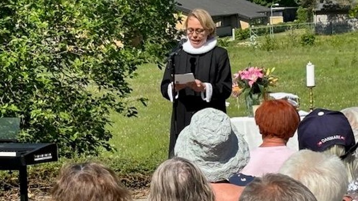 En kvinde i en have taler til et siddende publikum.