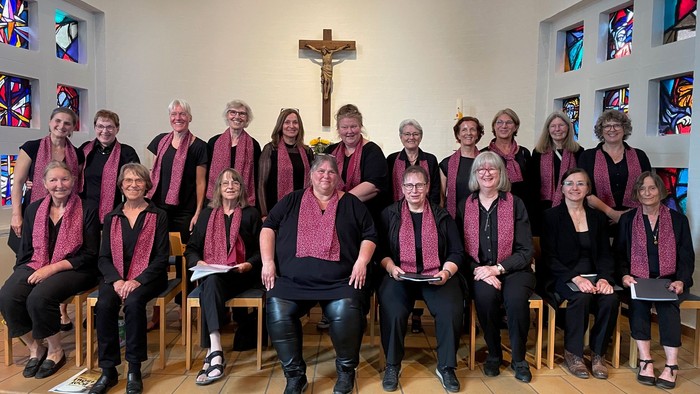 Eine Gruppe von Menschen in passenden weinroten Schals und schwarzer Kleidung posiert gemeinsam in einer Kirche.