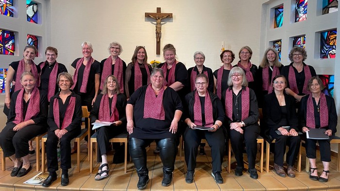 Eine Gruppe von Menschen in passenden weinroten Schals und schwarzer Kleidung posiert gemeinsam in einer Kirche.
