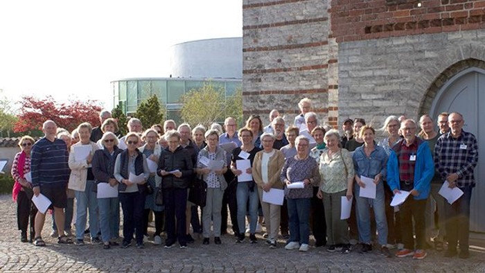 Gruppe af ældre mennesker, der står sammen udendørs, hver med et stykke papir i hånden.