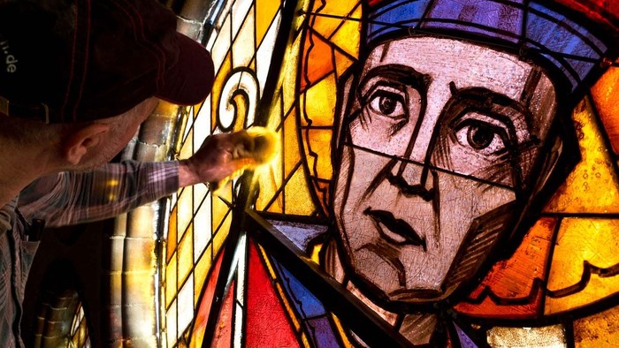 Mann arbeitet an einem buntem Glasfenster mit Abbildung eines Mannes