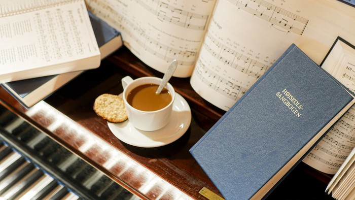 En kop kaffe og en kage på skrivebord med noter og bog