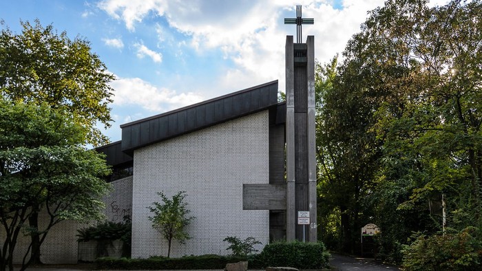 Moderne Kirche mit hohem Kreuz und umgeben von Bäumen