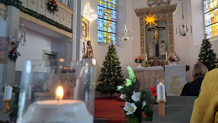 In der Kirche stehen Weihnachtsbäume, Kerzen und eine Kreuzigungsgruppe.
