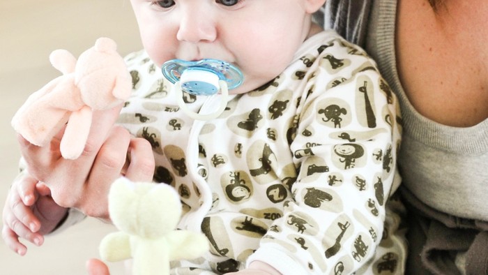 Et barn spiser fra en blå flaske, holdt af en voksende.