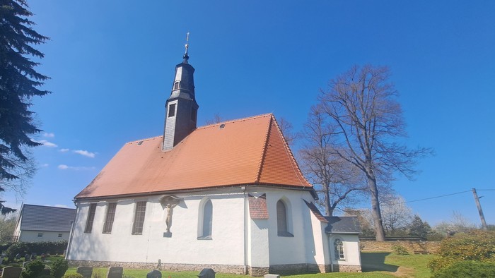 Kleine weiße Kirche mit rotem Dach und hohem Turm unter blauem Himmel
