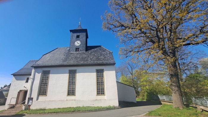 Weißes Kirchlein mit Uhrturm unter blauem Himmel