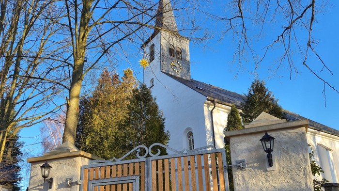 Eine friedvolle Kirche mit hohem Kirchturm, gesehen durch ein kunstvolles, holzgerahmtes Tor und eine Steinmauer.