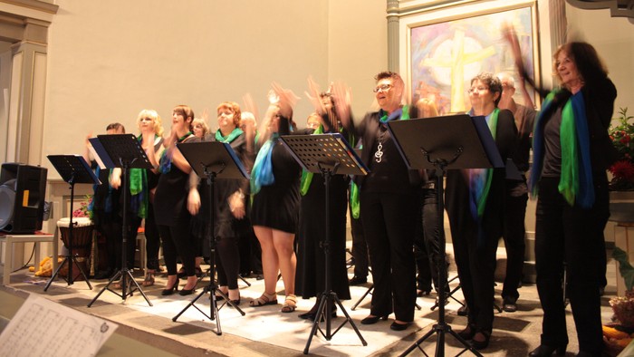 Ein Chor singt auf der Bühne mit Notenständern und Notenblättern.