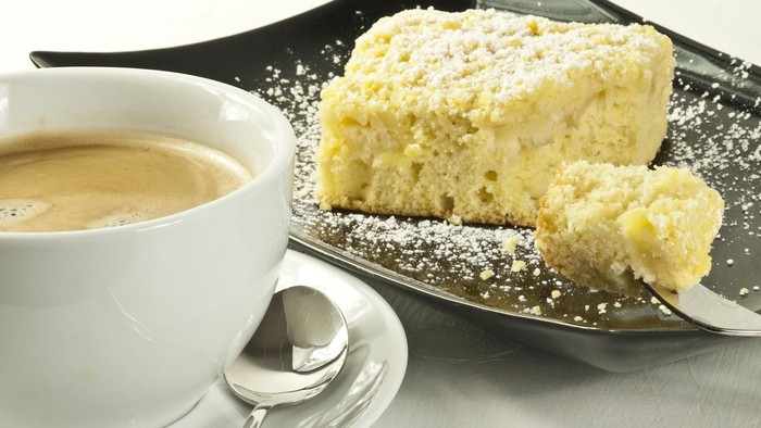 Eine Tasse Kaffee und ein Stück Kuchen auf einer Untertasse mit einem Löffel.