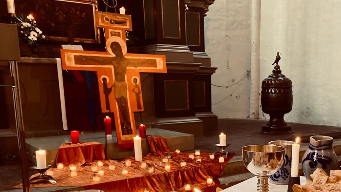 Ein Kirchenaltar mit einem großen Holzkreuz, Kerzen und einem Kelch.