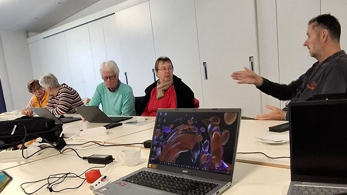 Eine Gruppe von Personen in einem Klassenzimmer mit Laptops und einem Vortragenden vorne.