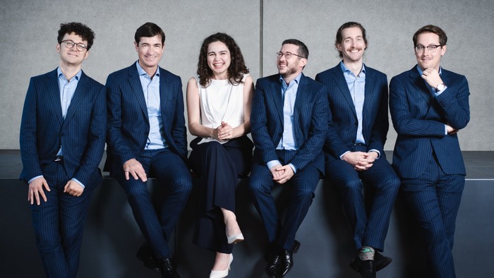 Professionelle Gruppe von sechs Personen in Businesskleidung, die selbstbewusst zusammen posieren.