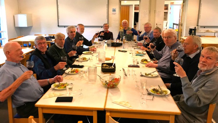 En gruppe ældre mænd sidder sammen og spiser sammen i en lokal.