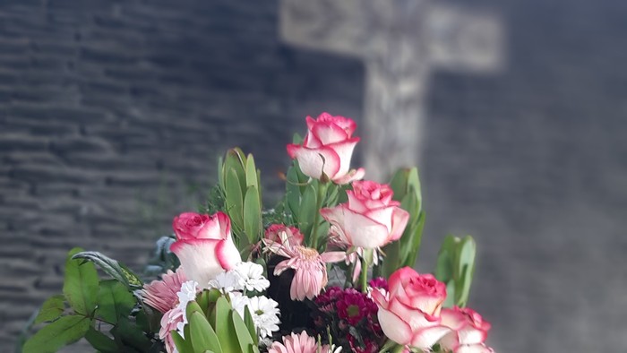 Blumenstrauß in Vase vor Kreuz an der Wand