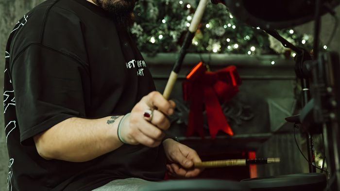 Zu sehen ist eine Detailaufnahme von Händen eines Schlagzeugers mit einer roten Schleife im Hintergurnd