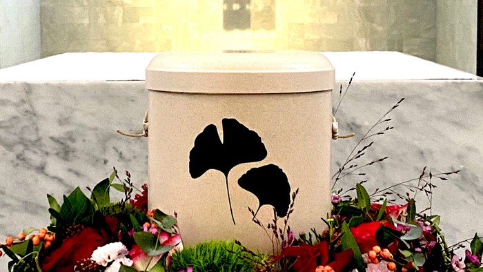 Elegante Gedenkurne mit Blumengirlande und Poinsettien-Muster, platziert auf einem Marmoraltar.