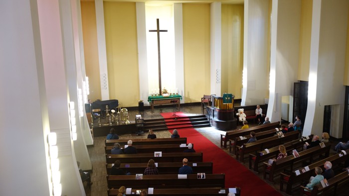 Die Kirche hat Holzbänke und einen Altar mit Kreuz.