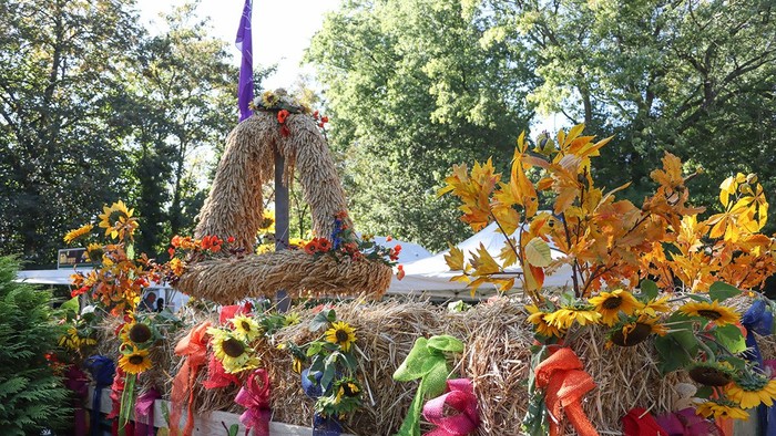 Ein bunter Erntekranz mit Sonnenblumen und bunten Bändern in einem Park.