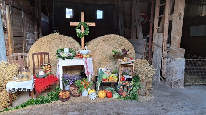 Ländliche Erntedekoration in einer Scheune mit Heuballen, Obst, Gemüse und einem dekorierten Tischaufbau.