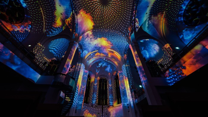Lebendige, farbenfrohe Lichtprojektionen erzeugen einen faszinierenden, futuristischen Kuppel-Effekt in einem imposanten architektonischen Raum.