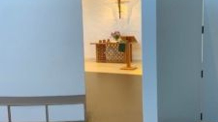 Moderne Kircheninnenraum mit weißen Wänden und hölzernem Kruzifix.