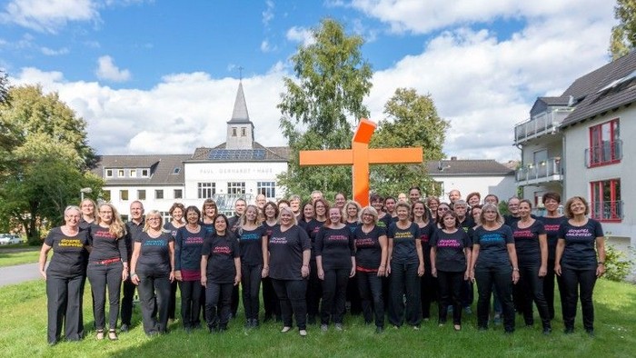 Gruppe von Personen, die vor einem großen Kreuz und Gebäuden posieren
